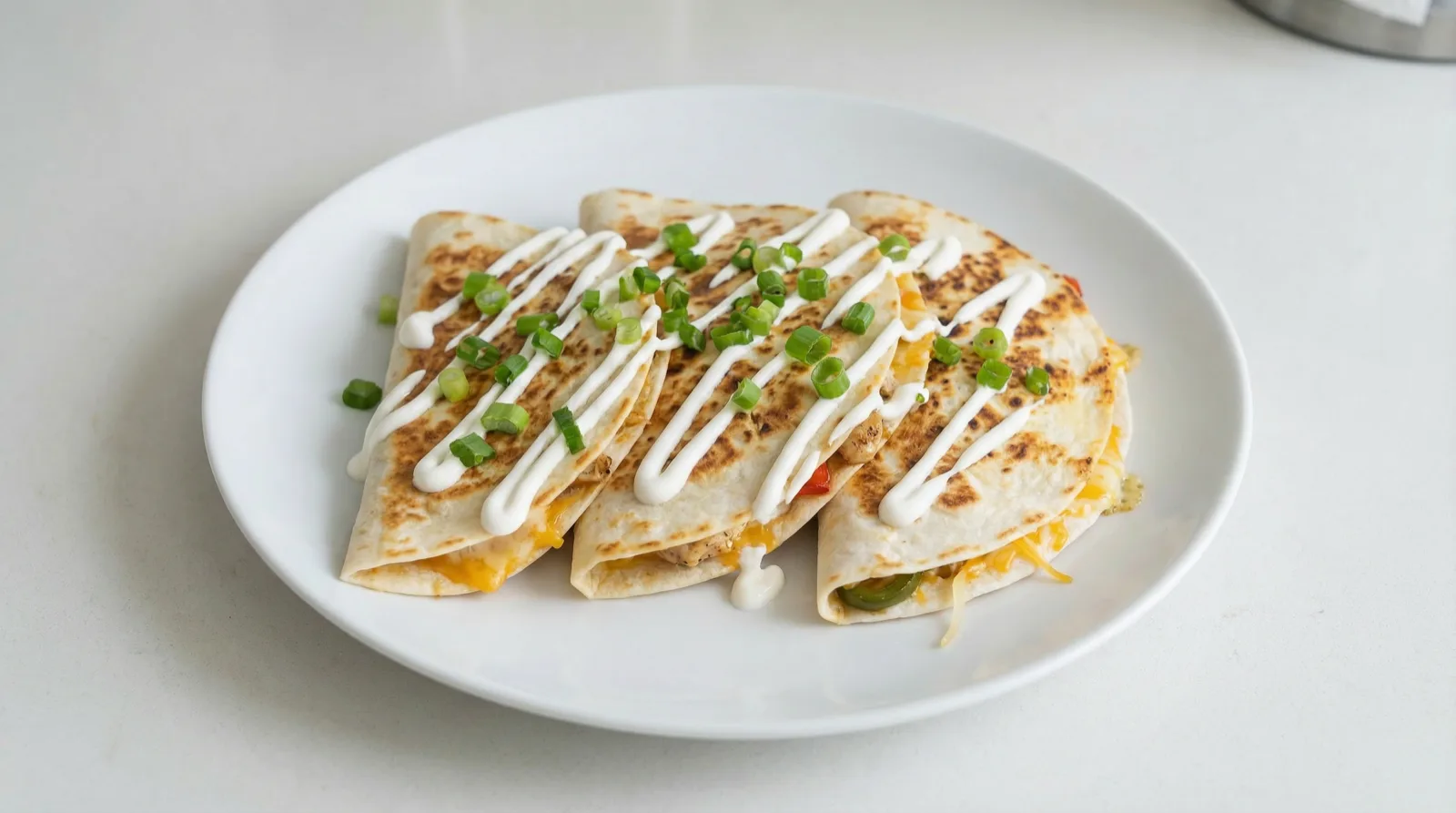 Three folded chicken quesadillas with sour cream and scallions on a white plate.